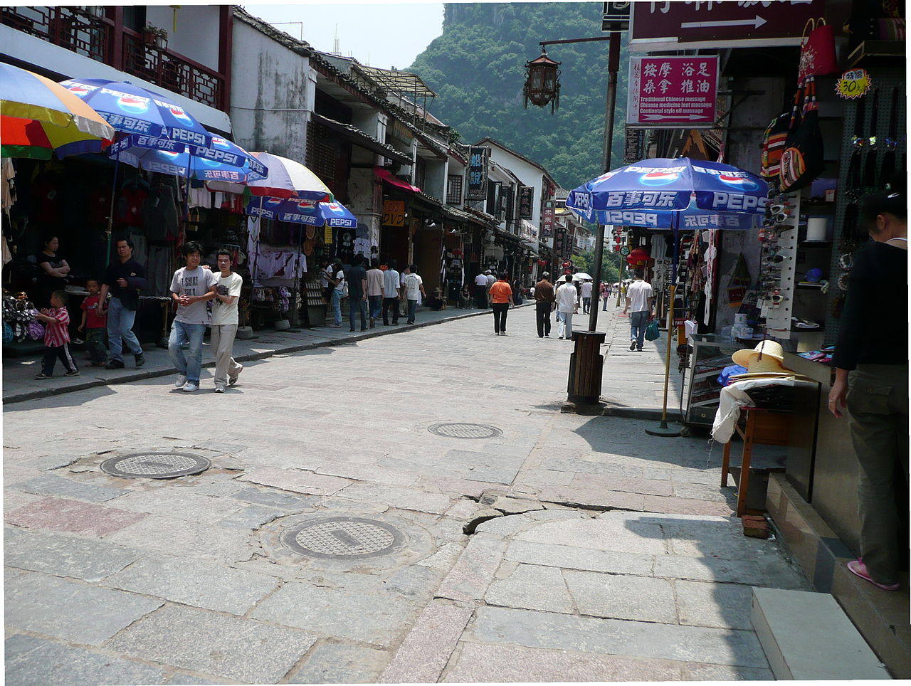 Busy pedestrian street with shops, umbrellas, and karst peaks in the background